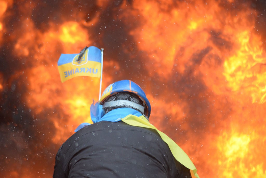 Protester_wearing_Ukraine_state_flag_colors_facing_the_massive_fire_set_by_protesters_to_prevent_internal_forces_from_crossing_the_barricade_line._Kyiv,_Ukraine._Jan_22,_2014