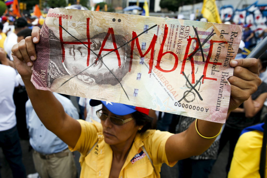 An opposition supporter holds up a giant hundred Bolivares note with the word, "Hungry" written on it during a gathering to protest against the government of Venezuela's President Nicolas Maduro, and economic insecurity and shortages, in Caracas August 8, 2015. (REUTERS/Carlos Garcia Rawlins)